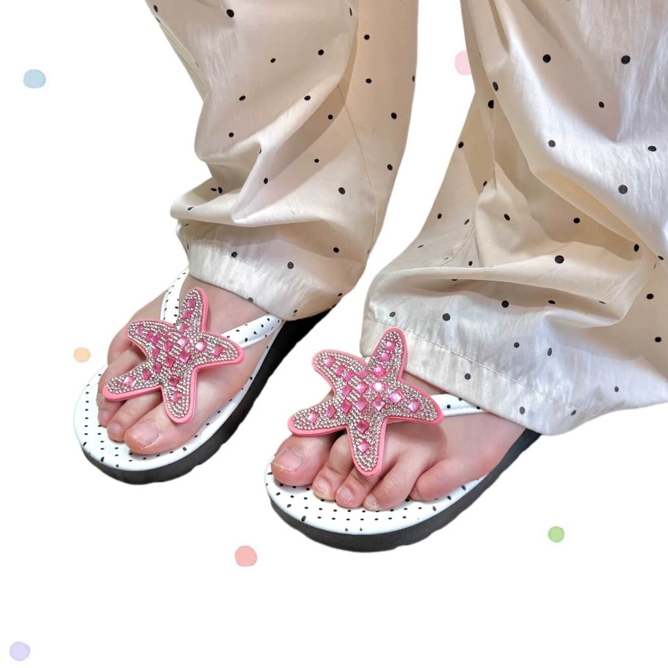 Pink starfish sandals worn with white pants featuring black dots on a white background