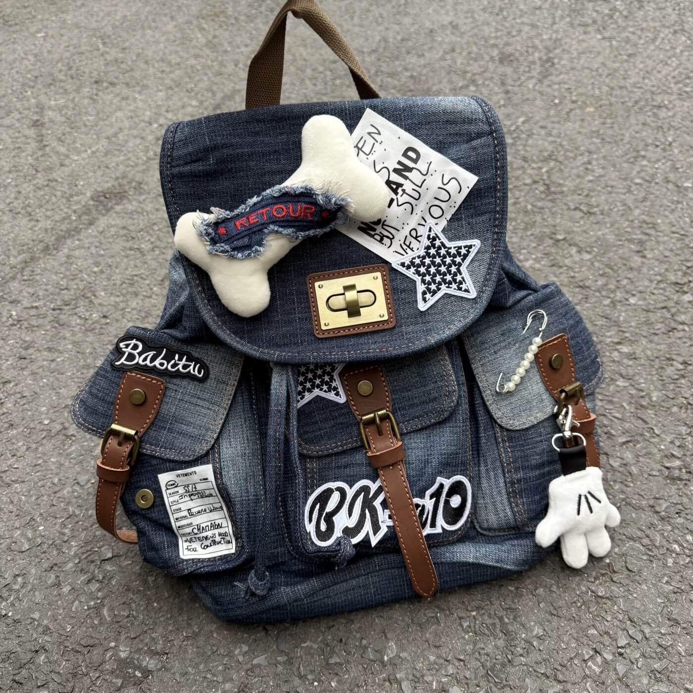 Denim backpack with patches and decorative items on a concrete surface