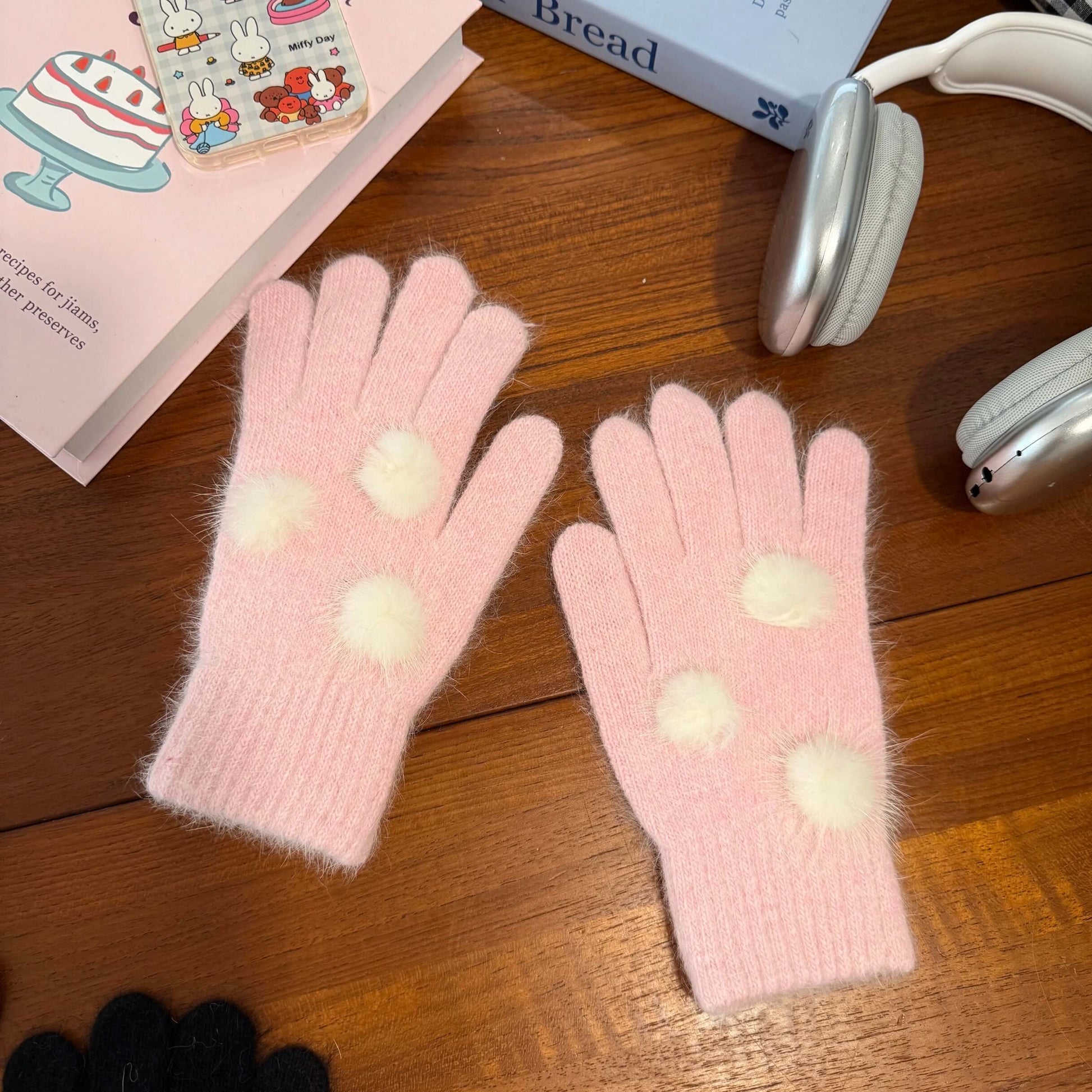 Soft pink knit gloves with white fuzzy pom poms for kawaii winter fashion.