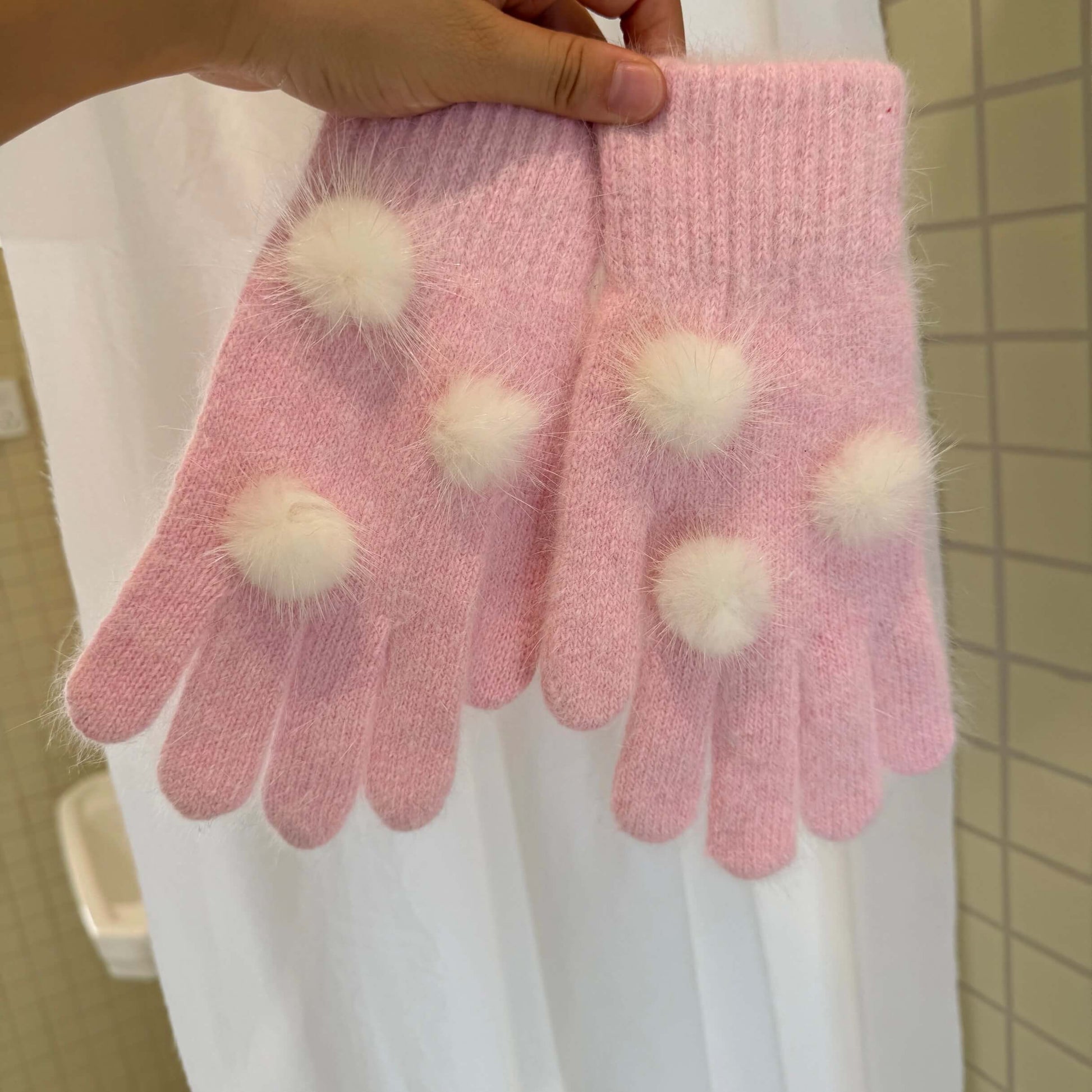 Soft pink knit gloves with white fuzzy pom poms for kawaii winter fashion.