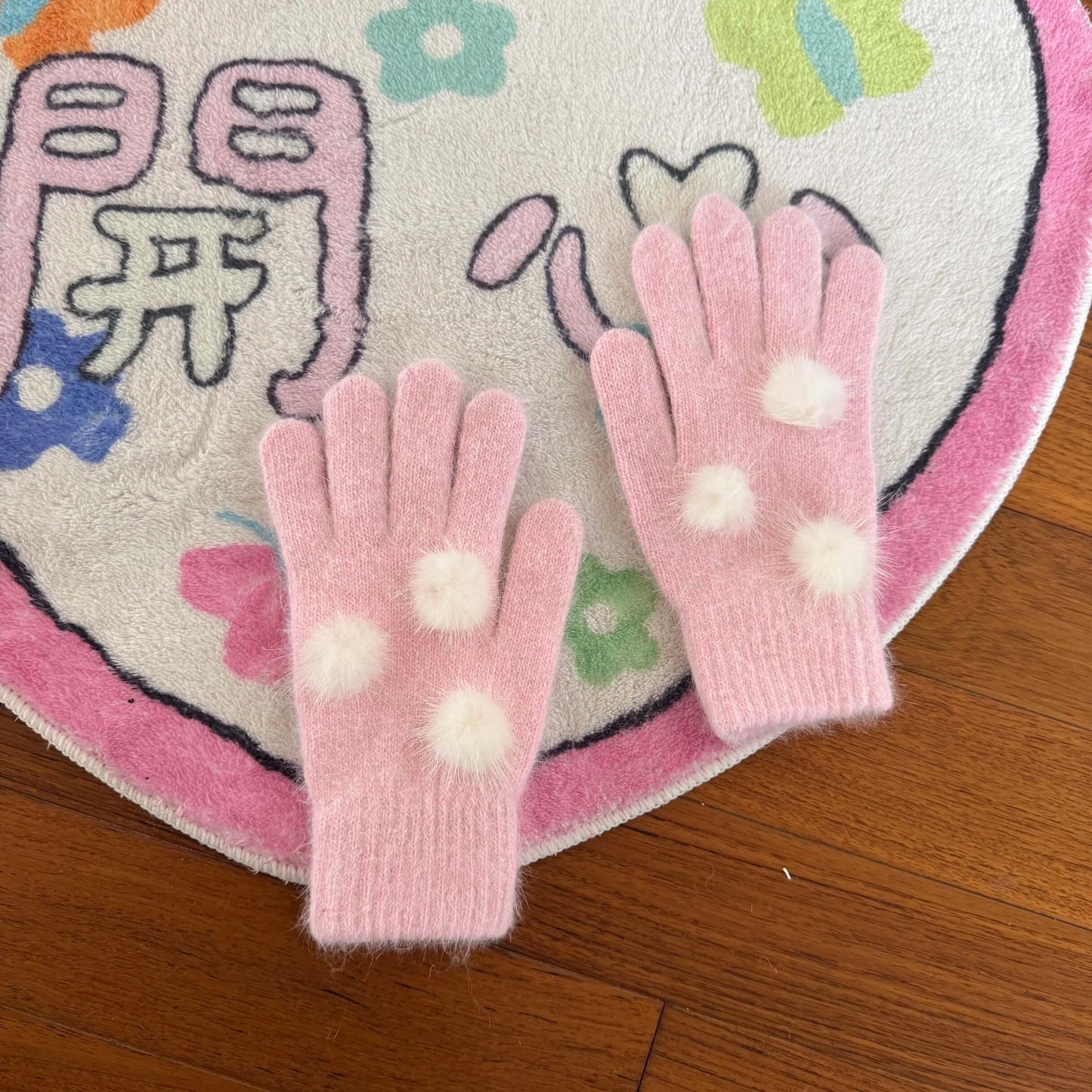 Soft pink knit gloves with white fuzzy pom poms for kawaii winter fashion.