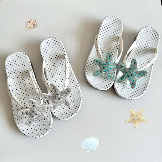 Pair of white sandals with starfish decorations on a light gray background