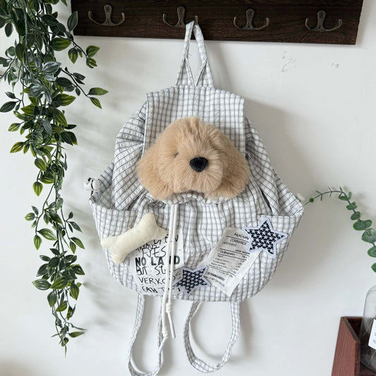 Checkered baby backpack with plush toy hanging on a hook against a white wall.