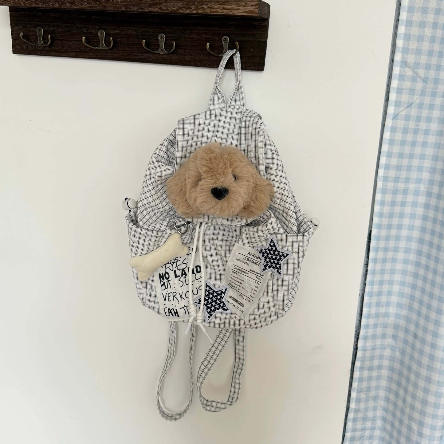 Small backpack with a teddy bear toy hanging on a hook against a white wall.