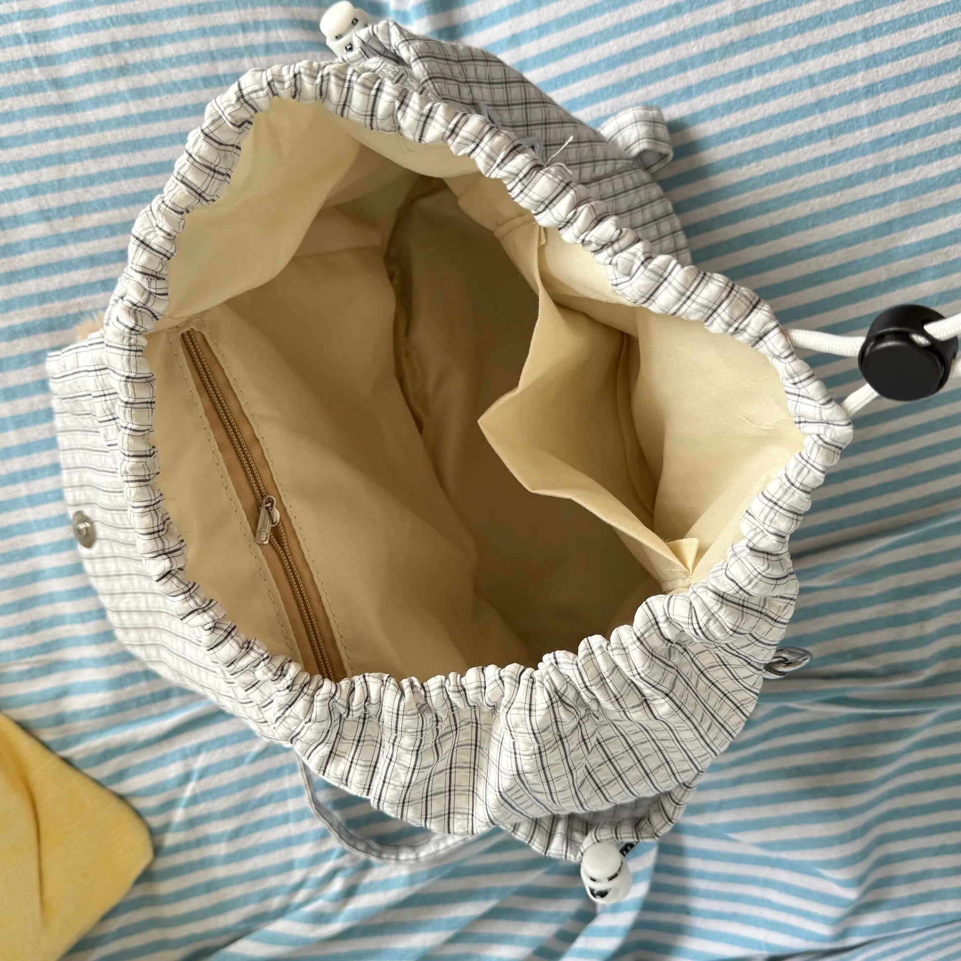 Textured fabric bag with beige interior on a blue and white striped background
