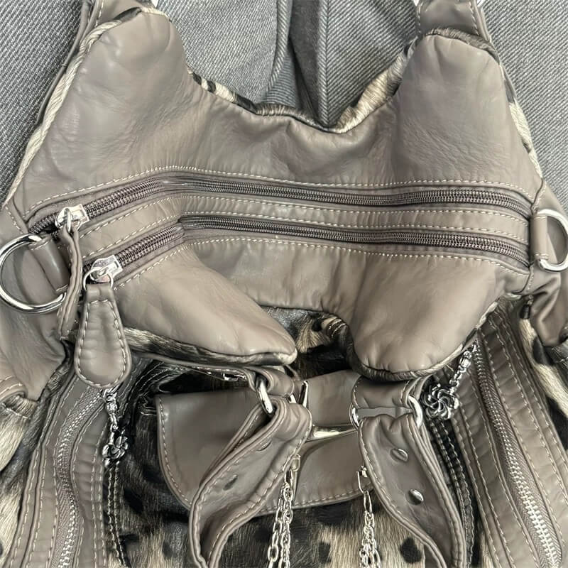 Close-up of a gray leather backpack with multiple zippers and chains.