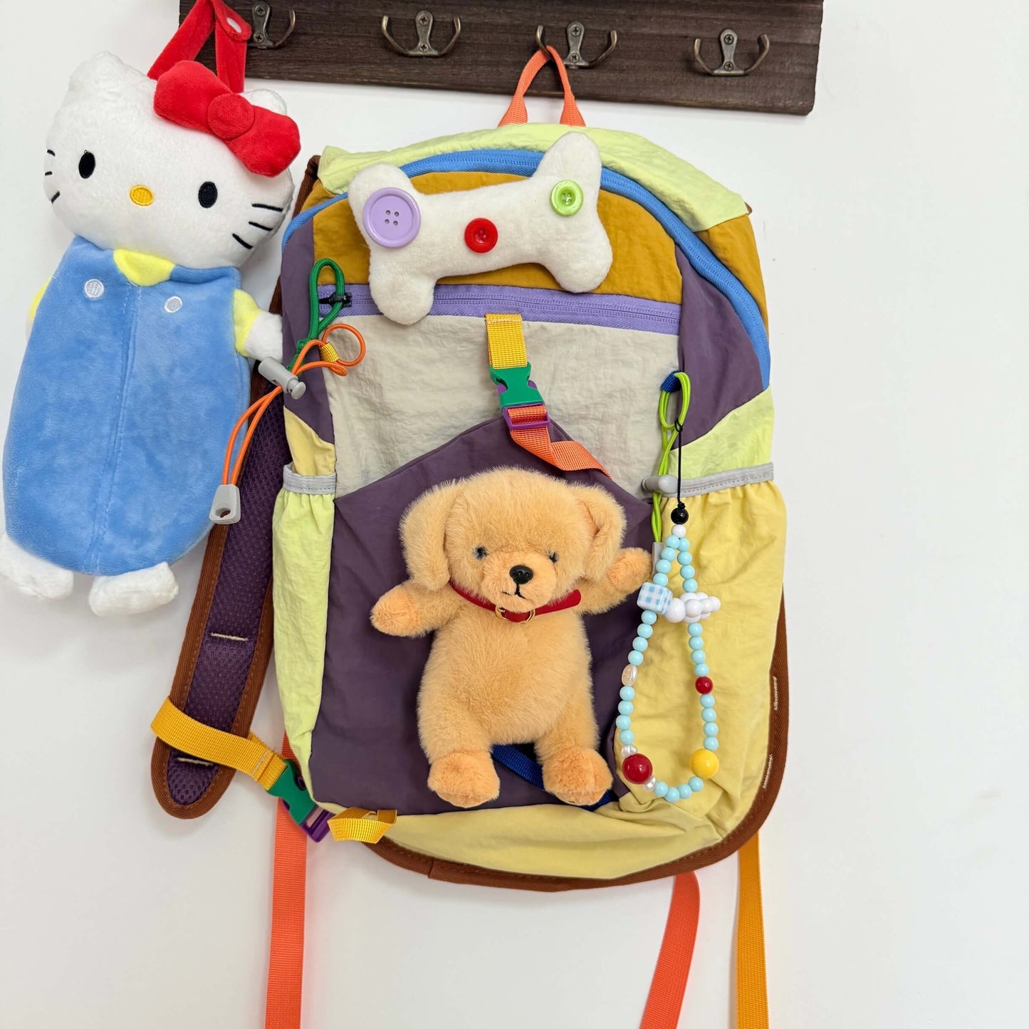 Colorful baby backpack with toys and a plush toy, hanging on a wall.