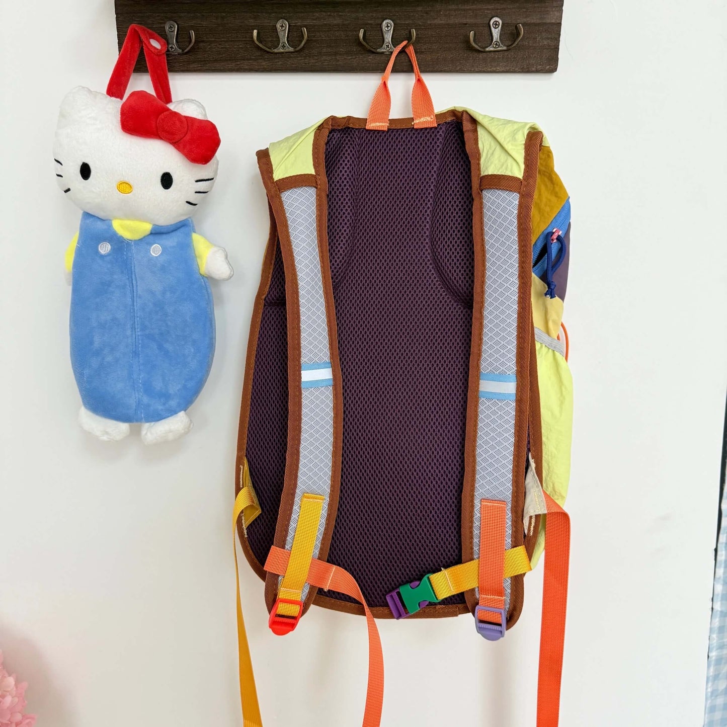Colorful children's backpack with a cartoon character hanging on a hook against a white wall.