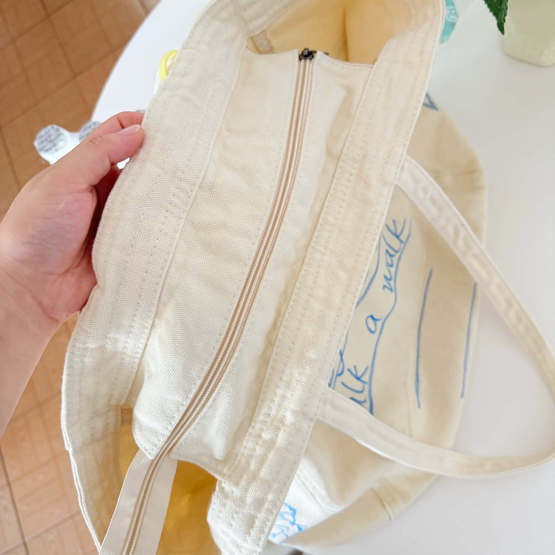 Close-up of a beige tote bag with text held by a hand on a blurred background